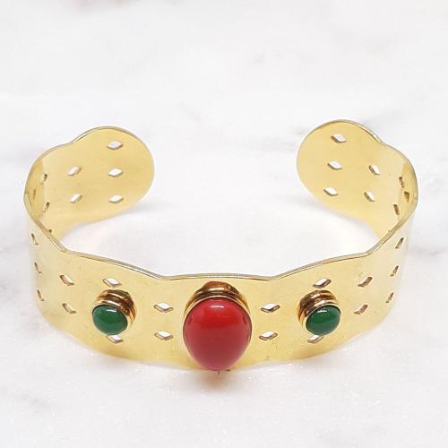 Ce bracelet manchette ajouré est en acier inoxydable doré avec une pierre rouge centrale et 2 pierres vertes latérales.